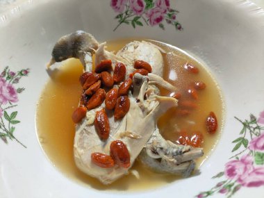 İçinde et ve kurt üzümü olan bir kase tavuk çorbası. Kâse beyaz ve pembe bir çiçek deseni var.