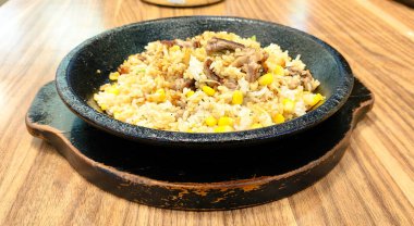 Üzerinde pirinç ve et olan Japon sıcak demir bir tabak yemek. Cızırdayan tabak ahşap bir masada, biberli soya soslu ızgara, teriyaki tavuğu veya sığır eti.