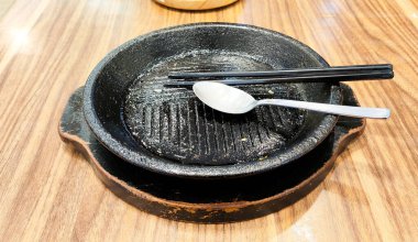 Üstünde kaşık ve yemek çubukları olan siyah bir Japon tencere levhası. Tava boş ve kaşık ters dönmüş.