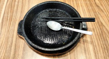 Üstünde kaşık ve yemek çubukları olan siyah bir Japon tencere levhası. Tava boş ve kaşık ters dönmüş.