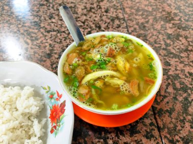 Bir tabak pirinç ve bir kase çorba soto kudus bir masada oturur. Çorba kasesi et ve sebzelerle kaplıdır. Pirinç tabağı beyaz ve üzerinde çatal ve kaşık var..