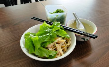 Yanında yemek çubukları ve kaşık olan bir kase yemek. Kasede erişte ve marul var.