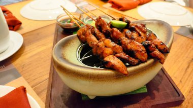 Sos soslu bir tabak et şişi. Tabak ahşap bir tahtanın üzerinde ve etrafı yemek çubuklarıyla çevrili.