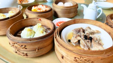 İçinde hamur köftesi ve çorba olan çeşitli Asya yemekleri olan bir masa. Masa çeşitli kâseler ve fincanlarla hazırlandı ve arka planda bir çaydanlık var. Çin doğulu Dim Sum