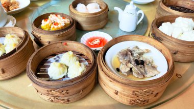 İçinde hamur köftesi ve çorba olan çeşitli Asya yemekleri olan bir masa. Masa çeşitli kâseler ve fincanlarla hazırlandı ve arka planda bir çaydanlık var. Çin doğulu Dim Sum