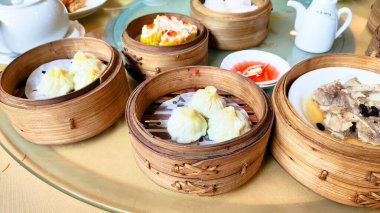 İçinde hamur köftesi ve çorba olan çeşitli Asya yemekleri olan bir masa. Masa çeşitli kâseler ve fincanlarla hazırlandı ve arka planda bir çaydanlık var. Çin doğulu Dim Sum