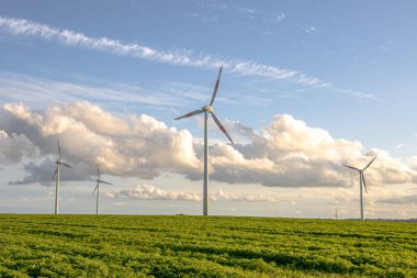 Rüzgar türbinleri açık bir alanda zarifçe dönerek teknolojiyi doğayla harmanlıyor. Bu yenilenebilir enerji kaynağı sürdürülebilirliği, temiz gücü ve daha yeşil, daha çevre dostu bir geleceğe olan bağlılığı simgeler..
