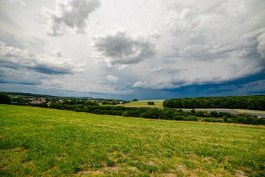 Karanlık bir hava ile yaz fırtınası yaklaşıyor ve derin mavi gökyüzünün altındaki yemyeşil alanlar üzerinde dramatik, yüksek kontrastlı bulutlar..