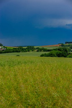 Karanlık bir hava ile yaz fırtınası yaklaşıyor ve derin mavi gökyüzünün altındaki yemyeşil alanlar üzerinde dramatik, yüksek kontrastlı bulutlar..