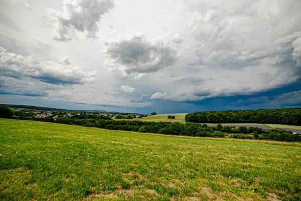 Karanlık bir hava ile yaz fırtınası yaklaşıyor ve derin mavi gökyüzünün altındaki yemyeşil alanlar üzerinde dramatik, yüksek kontrastlı bulutlar..