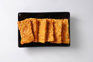 Kızarmış tempeh siyah bir tabakta servis edilir, izole edilmiş beyaz arka plan, geleneksel yiyecek konsepti