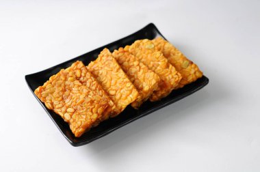 Kızarmış tempeh siyah bir tabakta servis edilir, izole edilmiş beyaz arka plan, geleneksel yiyecek konsepti