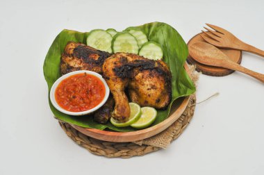 Muz yapraklarıyla kaplı ahşap tabakta acı soslu ızgara tavuk.