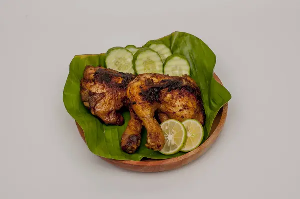Grilled chicken with chili sauce on a wooden plate lined with banana leaves