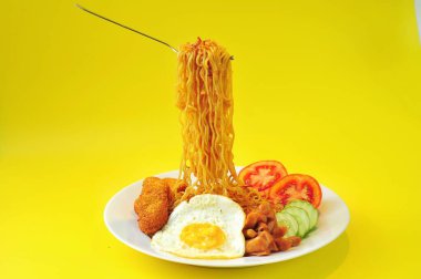 fried noodles, fried eggs, tomatoes slice, cucumber, nuggets on white plate, yellow background clipart