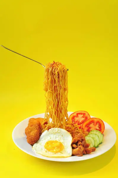 fried noodles, fried eggs, tomatoes slice, cucumber, nuggets on white plate, yellow background