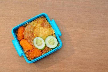 Kızarmış pirinç, nugget ve kızarmış erişte içeren yemek kutusu, ahşap bir masanın üzerinde.