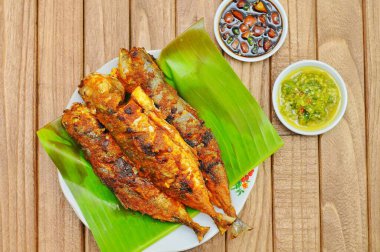 Ikan Bakar veya muz yaprağı ve izole ahşap arka planda servis edilen Endonezya baharatlı ızgara balık.