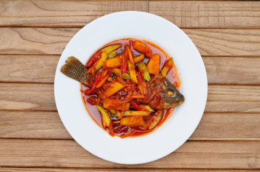 Kızarmış Tilapia Balığı üzerine tatlı ve ekşi sos, beyaz tabakta servis edilir.