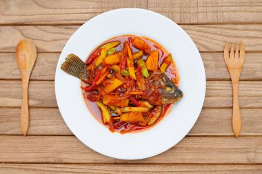 Kızarmış Tilapia Balığı üzerine tatlı ve ekşi sos, beyaz tabakta servis edilir.