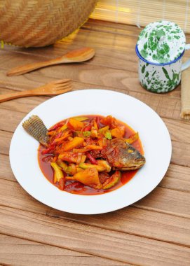 Kızarmış Tilapia Balığı üzerine tatlı ve ekşi sos, beyaz tabakta servis edilir.