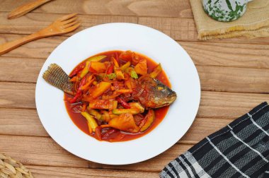 Kızarmış Tilapia Balığı üzerine tatlı ve ekşi sos, beyaz tabakta servis edilir.