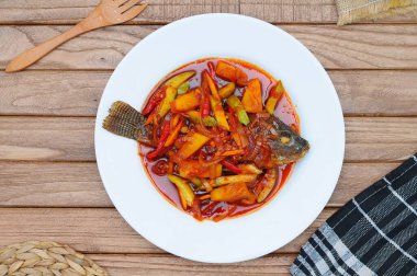 Kızarmış Tilapia Balığı üzerine tatlı ve ekşi sos, beyaz tabakta servis edilir.