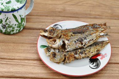 Kızarmış uskumru beyaz bir tabakta ve ahşap bir masada servis edilir.