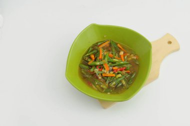 Kızarmış yeşil fasulye ve havuç, ahşap bir masada yeşil bir kasede servis edilir.