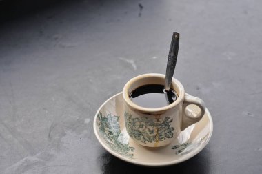 Bir fincan kahve ve siyah arka planda bir kaşık.