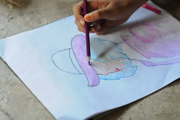 A child\'s hands are coloring his work