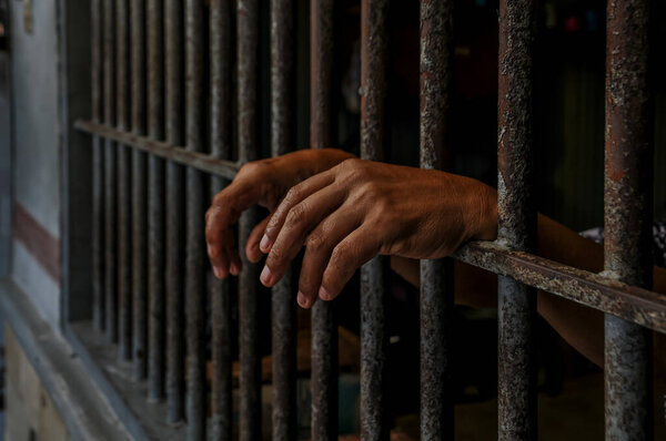 hands of a prisoner behind prison bars