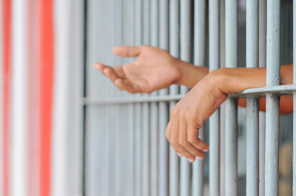 hands of a prisoner behind prison bars on black background