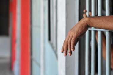 Mahkûmun elleri siyah arka planda parmaklıklar ardında.