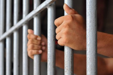 Mahkûmun elleri siyah arka planda parmaklıklar ardında.