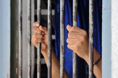 Mahkûmun elleri siyah arka planda parmaklıklar ardında.