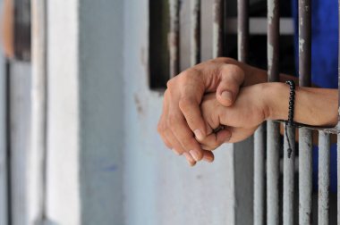 Mahkûmun elleri siyah arka planda parmaklıklar ardında.