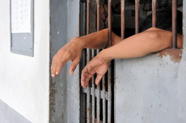 Mahkûmun elleri siyah arka planda parmaklıklar ardında.