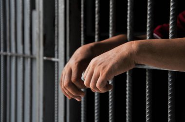 Mahkûmun elleri siyah arka planda parmaklıklar ardında.