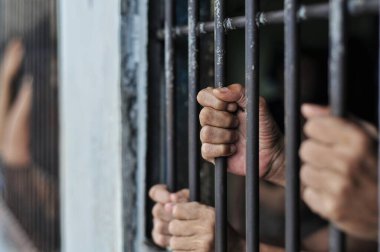 Mahkûmun elleri siyah arka planda parmaklıklar ardında.