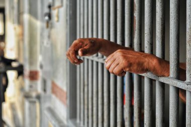 Mahkûmun elleri siyah arka planda parmaklıklar ardında.