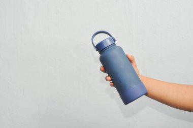 Adamın eli, arka planı duvarla çevrili bir su bardağını tutuyor.