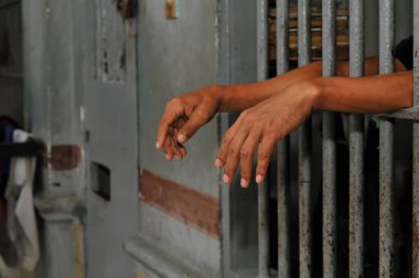 Mahkûmun elleri siyah arka planda parmaklıklar ardında.