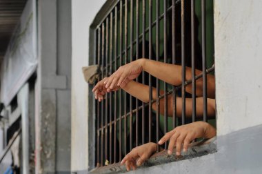 Mahkûmun elleri siyah arka planda parmaklıklar ardında.