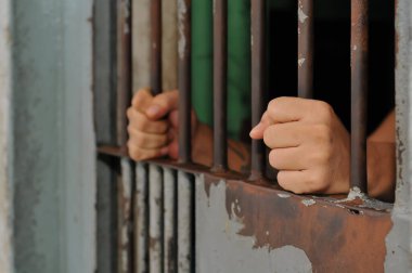 Mahkûmun elleri siyah arka planda parmaklıklar ardında.