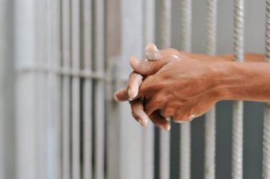 Karanlık bir hücrede parmaklık tutan bir mahkumun yakın çekimi. Hapis, ceza, hapsedilme ve ceza adaleti kavramı.