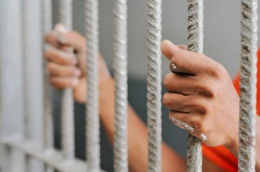 Karanlık bir hücrede parmaklık tutan bir mahkumun yakın çekimi. Hapis, ceza, hapsedilme ve ceza adaleti kavramı.