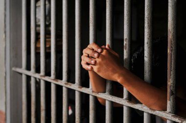 Karanlık bir hücrede parmaklık tutan bir mahkumun yakın çekimi. Hapis, ceza, hapsedilme ve ceza adaleti kavramı.