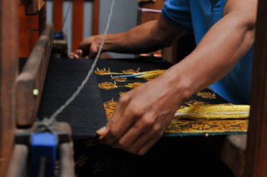 Zanaatkar ellerin ahşap bir dokuma tezgahında altın iplikle geleneksel kumaş dokuması. Kültürel el yapımı tekstil ve zanaat ayrıntıları.
