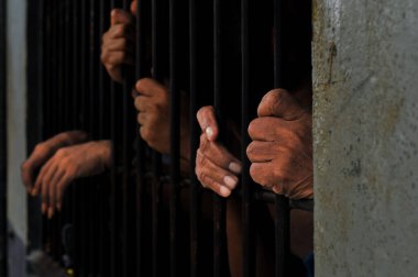 Karanlık bir hücrede parmaklık tutan bir mahkumun yakın çekimi. Hapis, ceza, hapsedilme ve ceza adaleti kavramı.